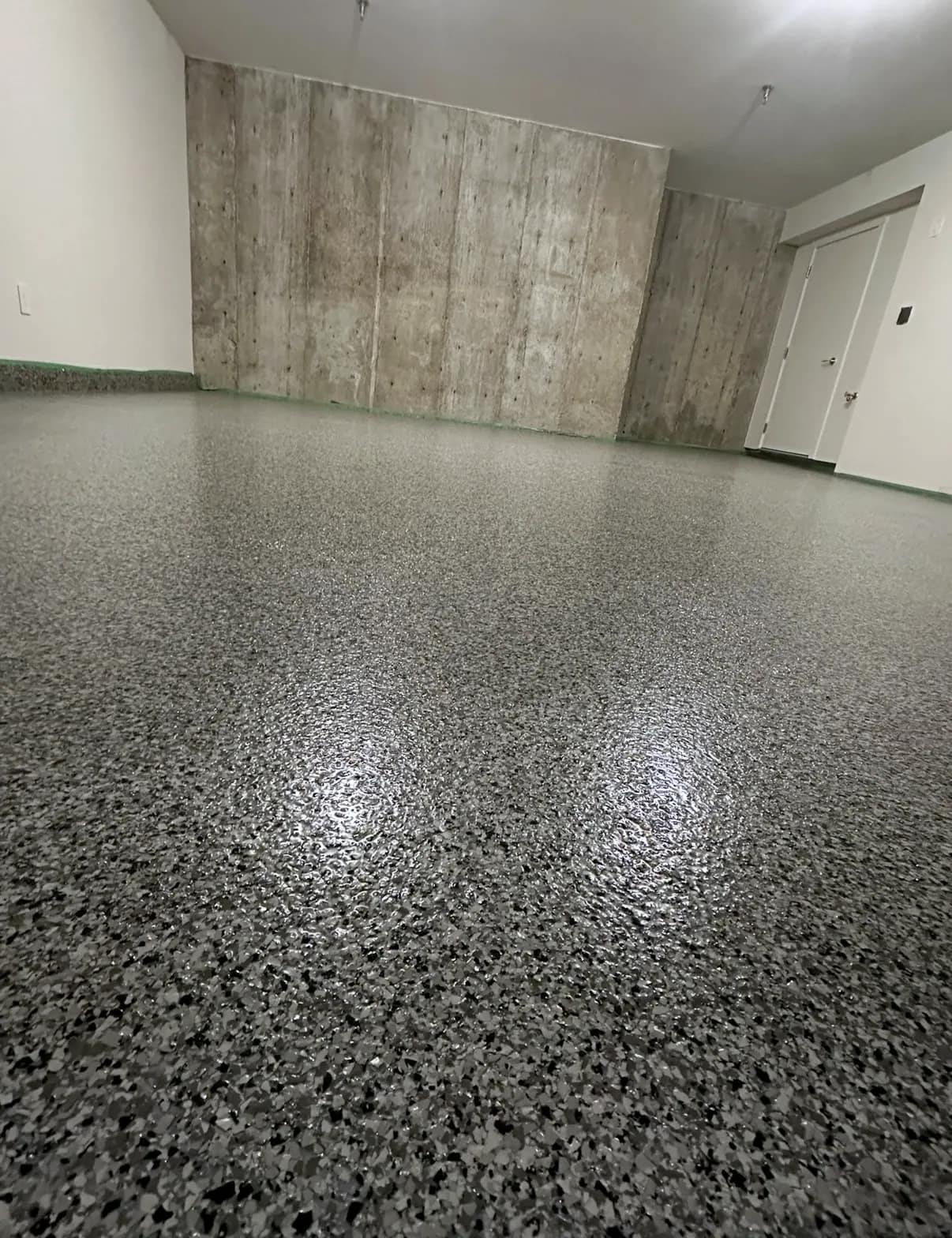 Basement room with a grey flake epoxy floor running up to a board-formed concrete wall