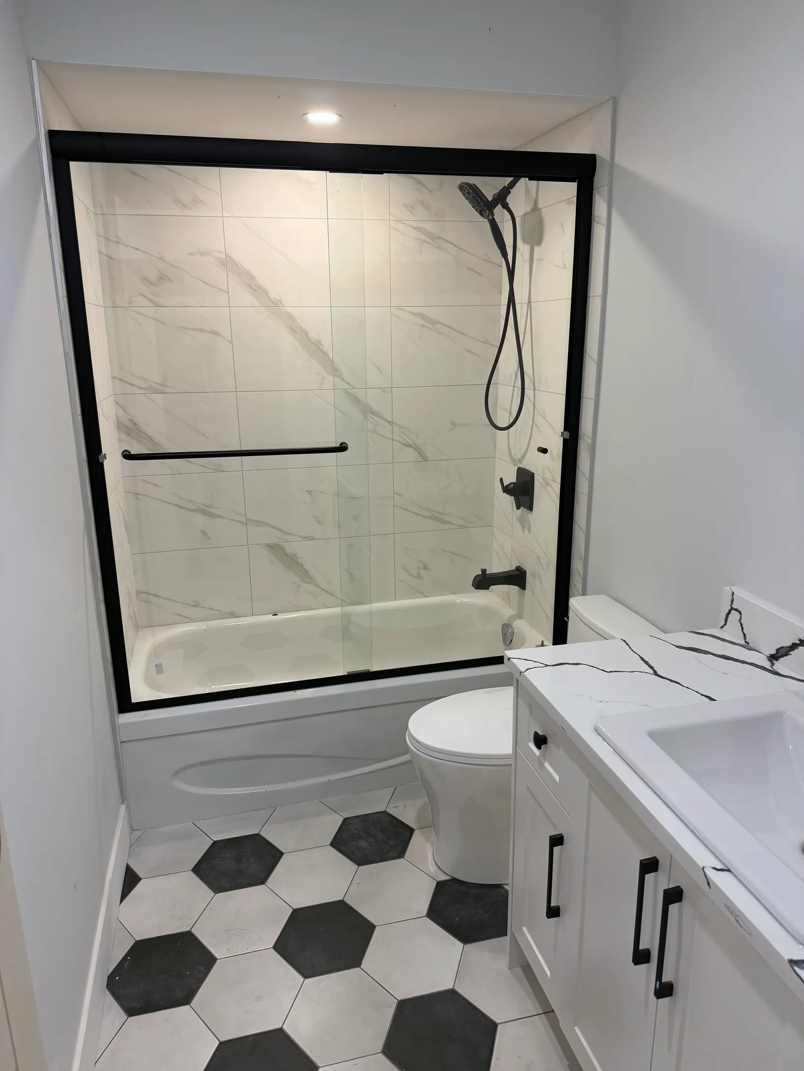 Finished bathroom with a marble-look tiled tub surround, black fixtures and a black and white hexagon tile floor
