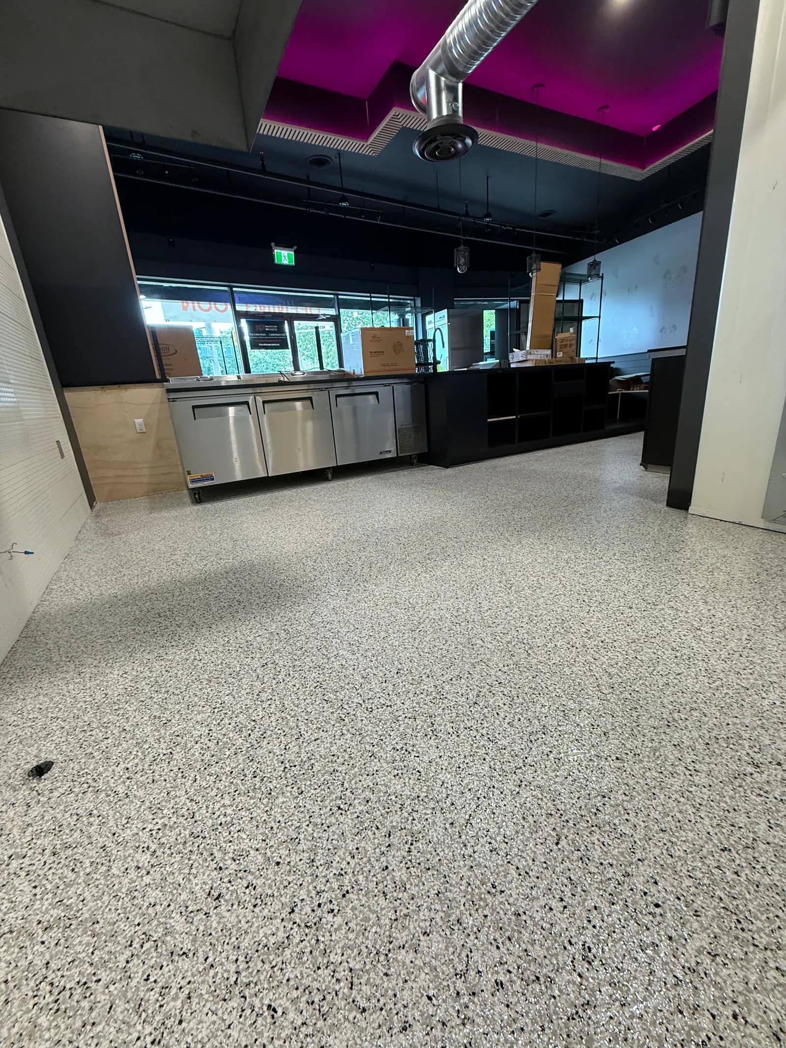 Commercial food service area with a pale speckled flake floor running under stainless prep counters