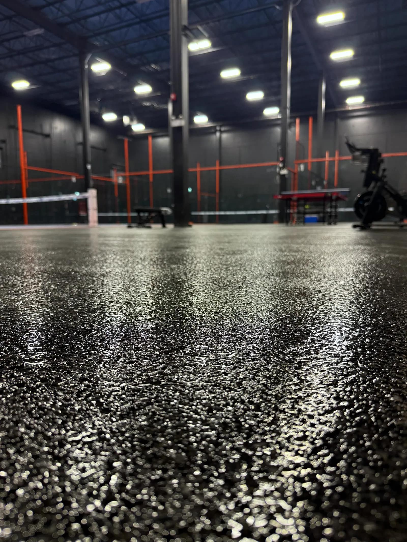 Dark flake epoxy floor running the length of a large gym, with orange rigging in the background