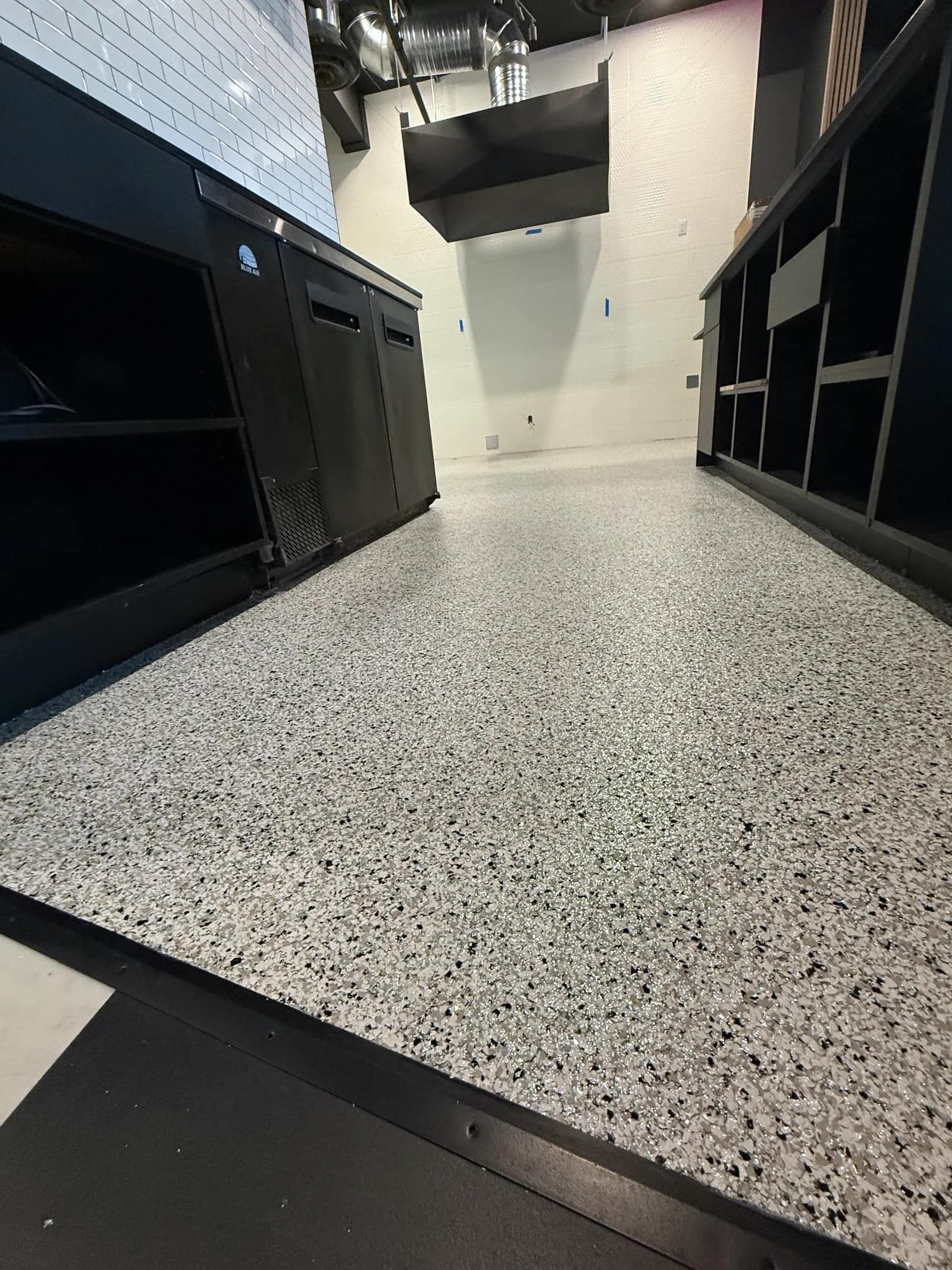 Commercial kitchen with a white and black flake floor running under stainless steel coolers