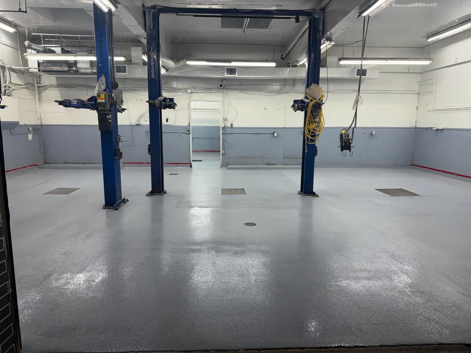 Automotive service bay with three two-post hoists standing on a light grey solid-colour epoxy floor