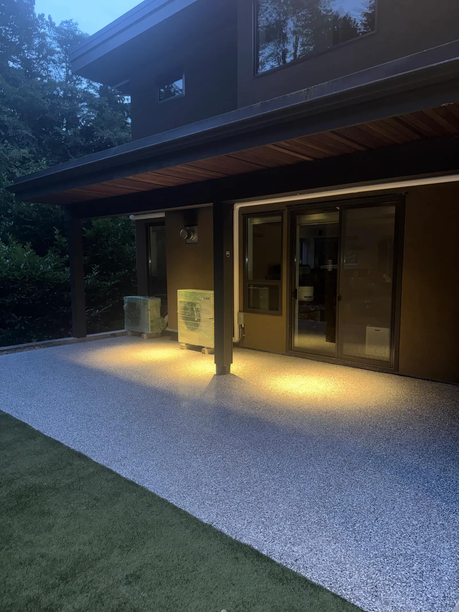 Covered patio at dusk with a pale flake coating lit by downlights above the sliding doors