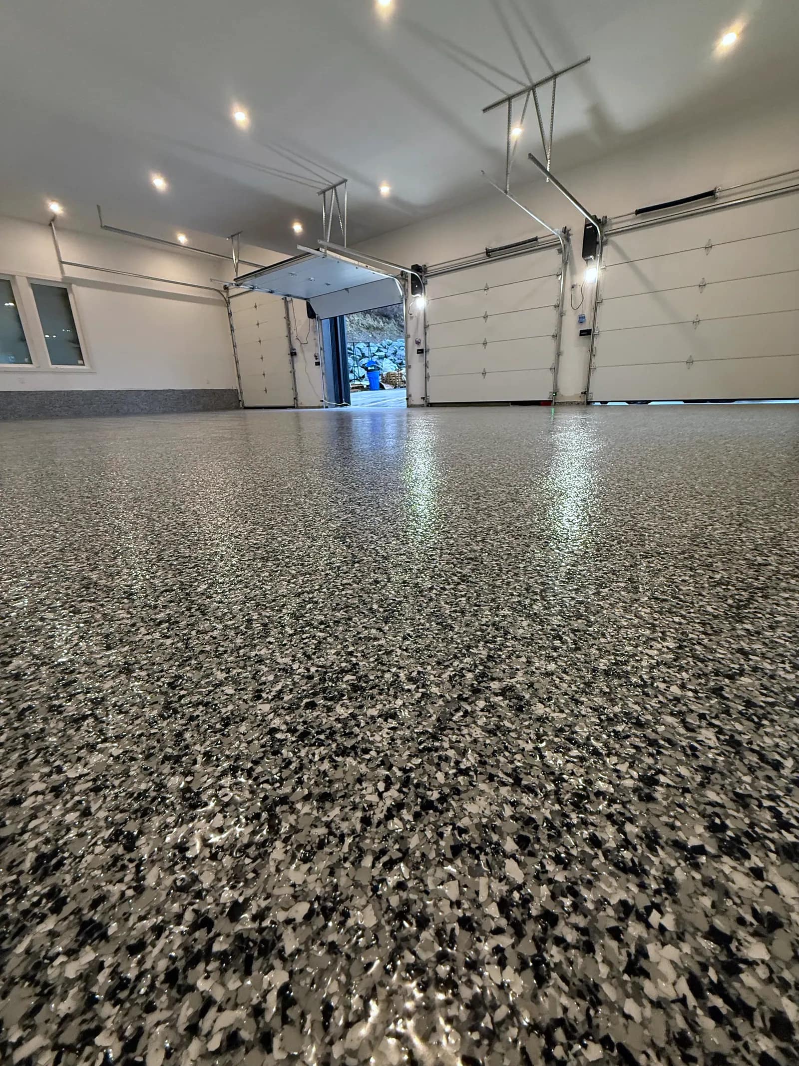 Residential double garage with a glossy charcoal flake epoxy floor reflecting the ceiling lights