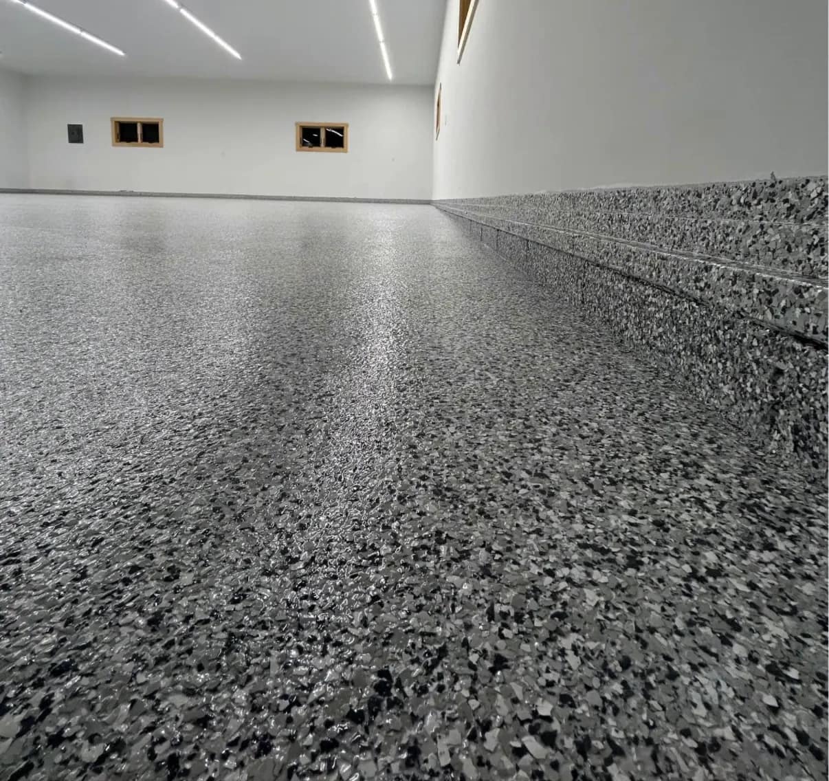 Wide empty room with a grey and black flake epoxy floor and a matching coved base running up the wall