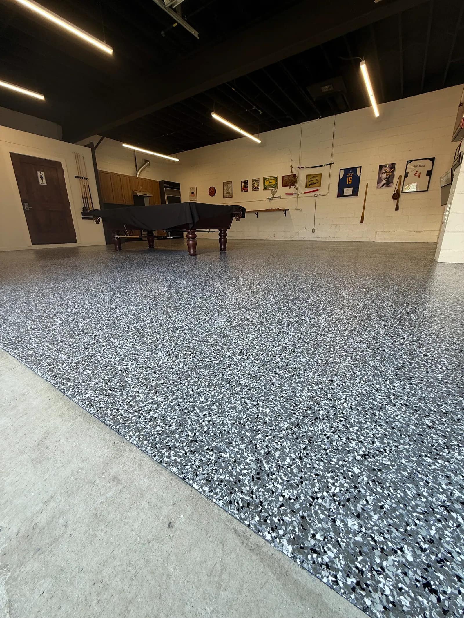 Large shop interior with a pool table standing on a black and white flake epoxy floor