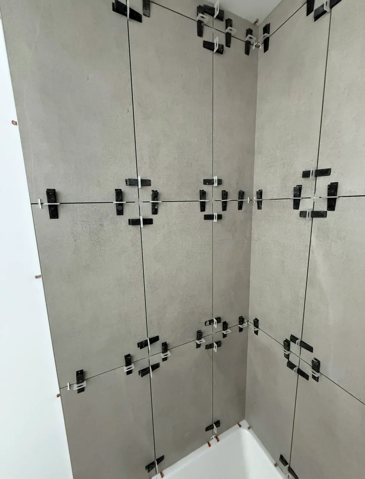 Corner of a shower enclosure tiled in large grey concrete-look tile with levelling clips and spacers fitted