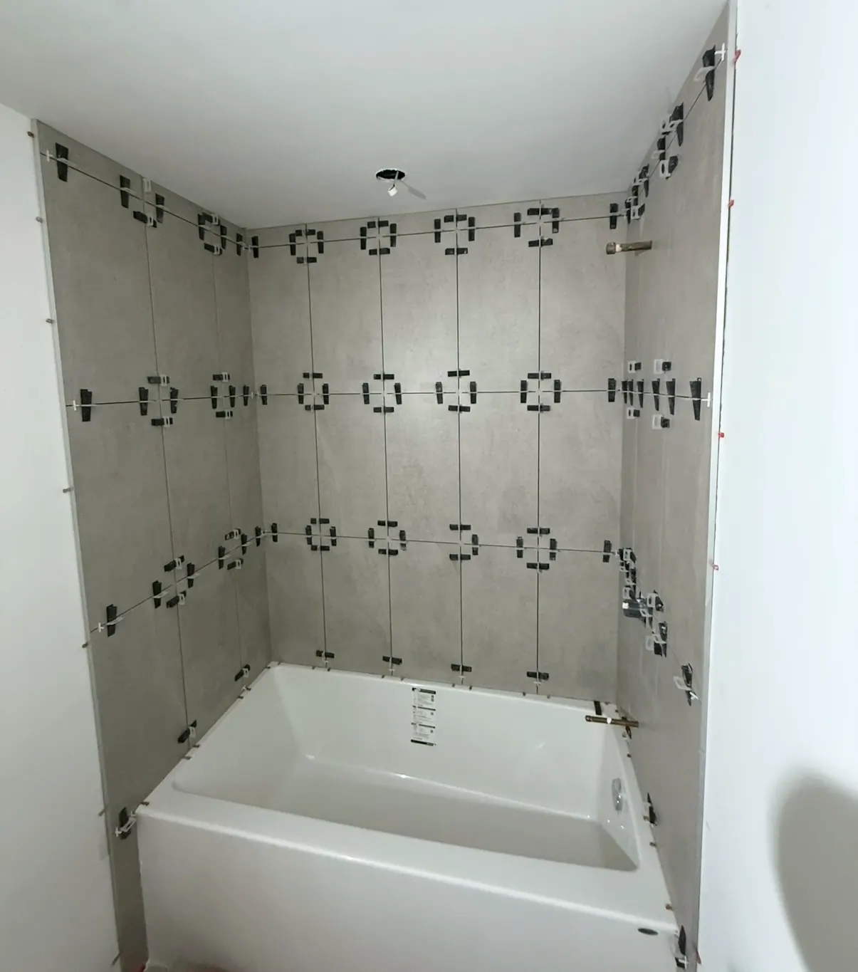 Tub surround part-tiled in large grey concrete-look tile, with levelling clips still in place